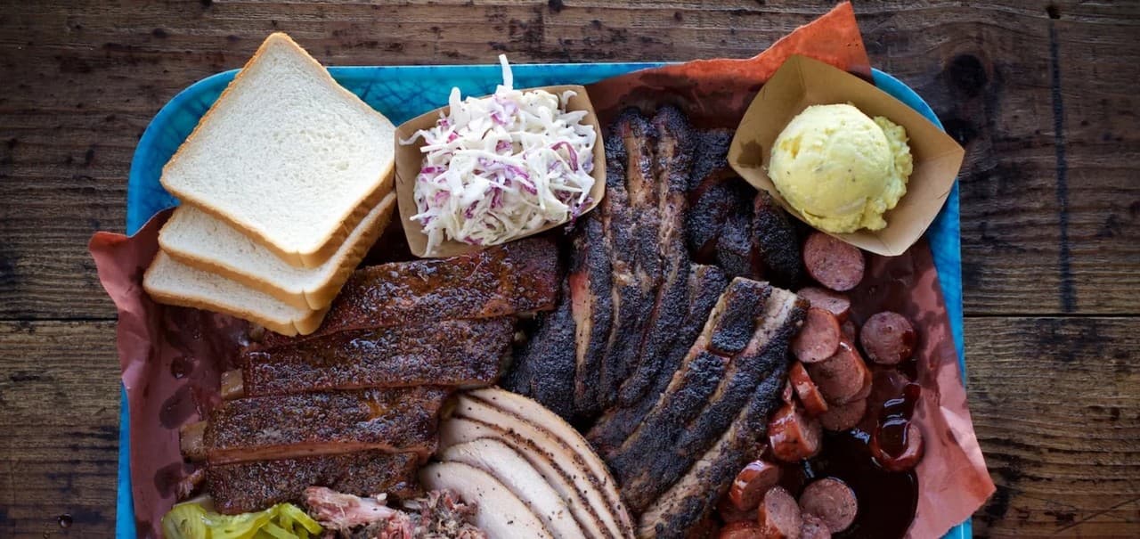 Overhead view of a Franklin Barbecue platter with smoked meats, bread, coleslaw, and sides