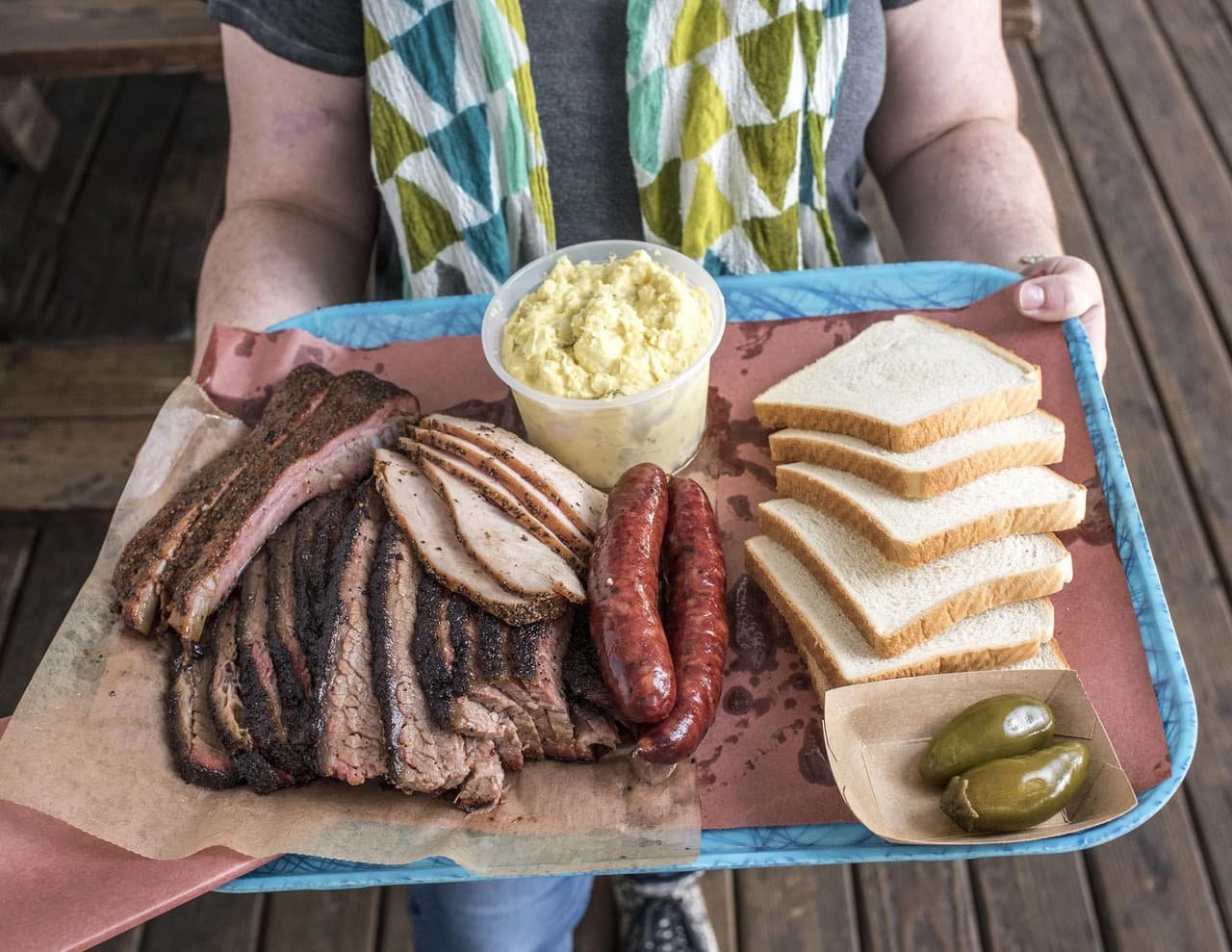 A full tray of Franklin Barbecue brisket, sausage, bread, and sides enjoyed on a porch